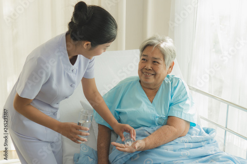 Konstfotografi caregiver nurse helping elderly woman taking medicine on the bed and check up after admit inpatient in hospital