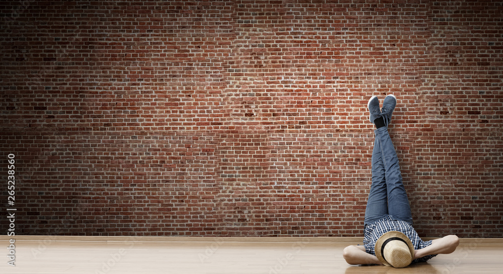 Obraz premium Young man lying on the floor with legs raised up on the wall. Mixed media