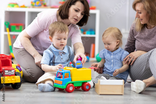 Nursery kids playing with toys. Mothers communicate and watch over their children