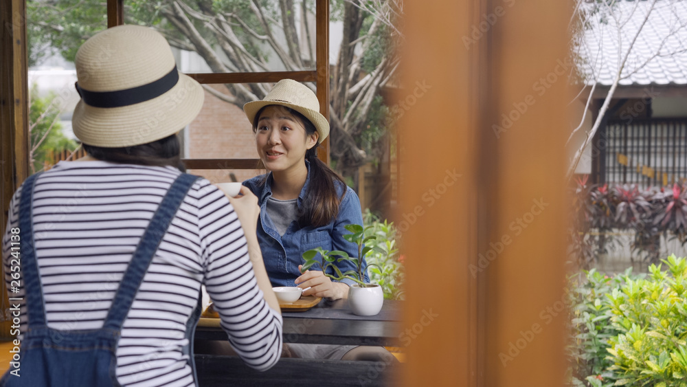 shocked asian woman sitting by wooden table with her friends talking back camera. young girls surprised open eyes big listening to sister. female tourists trying chado japanese culture tea ceremony.