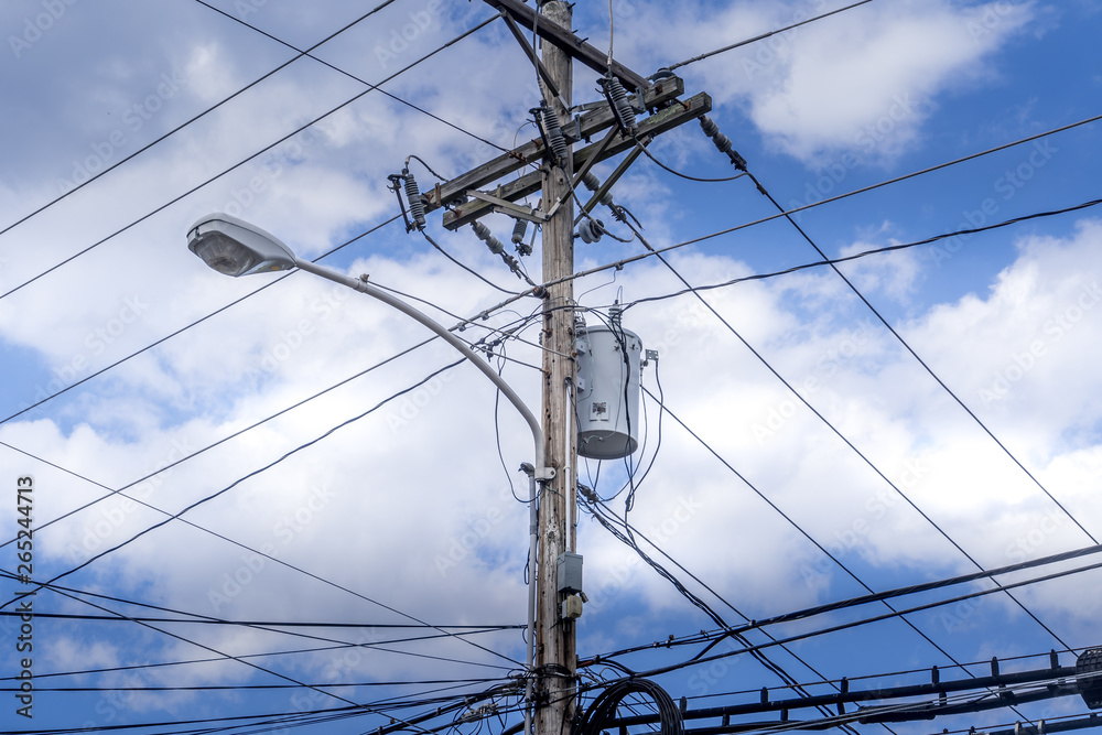 Rustic wooden telephone pole with electric wires and street lamp with blue cloudy sky background