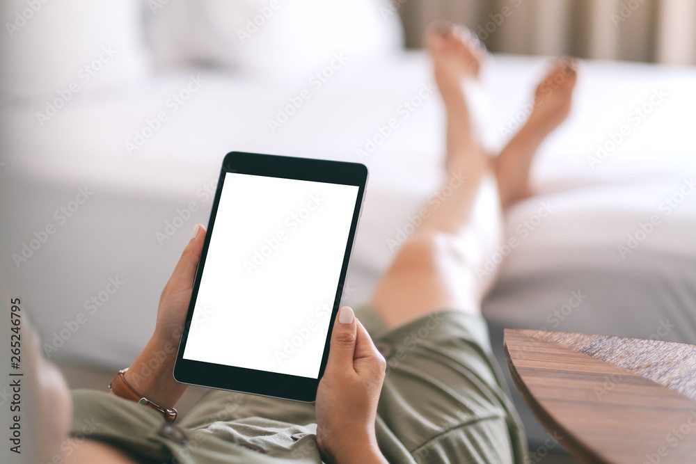 Mockup image of a woman holding and using tablet pc with blank screen while relaxing and lying on the bed Mockup image of a woman holding and using tablet pc with blank screen while relaxing and lying on the bed