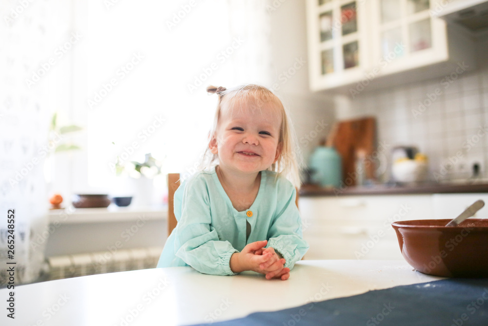 Cute Toddler blonde girl sitting in the kitchen - obrazy, fototapety, plakaty 
