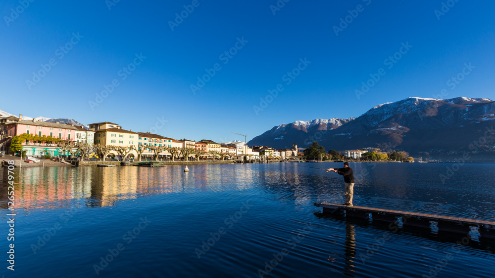 Ascona Lake Maggiore 2 December 2012: Man holds long fishing rod and fishes at lake surrounded by beautiful countryside