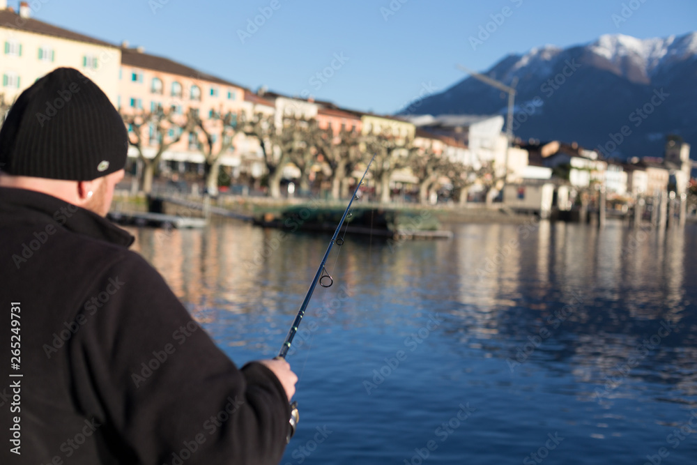 Ascona Lake Maggiore 2 December 2012: Man holds long fishing rod and fishes at lake surrounded by beautiful countryside