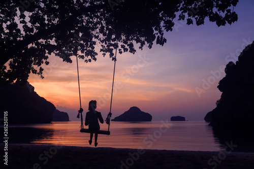 Silhouette of a girl sitting on a swing or cradle on the beach at sunset.