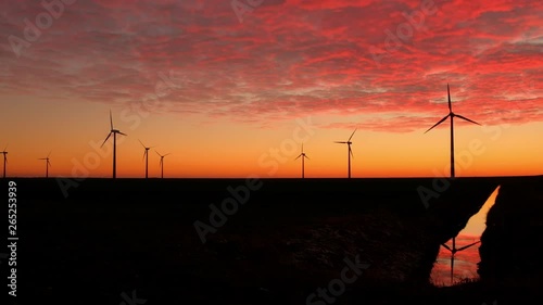 Wind Turbines Generating Green Energy at Sunset with Reflection in a Canal and Beautiful Red Clouds in the Sky in Almere Pumpus, Netherlands photo