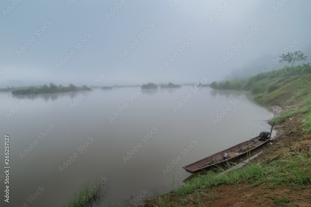 River view misty morning of a small fishing boat floating in Mekong river around with soft mist in the sky background, Ban Muang, Sang Khom District, Nong Khai, Thailand.