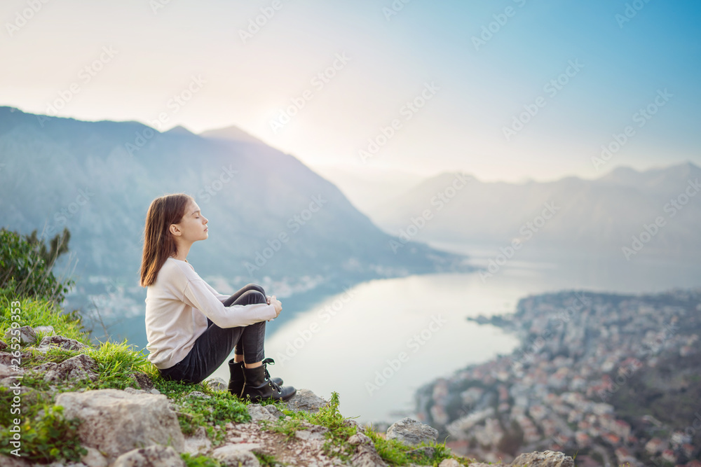 Child girl sitting with closed eyes above the mountain valley in a light of sunrise