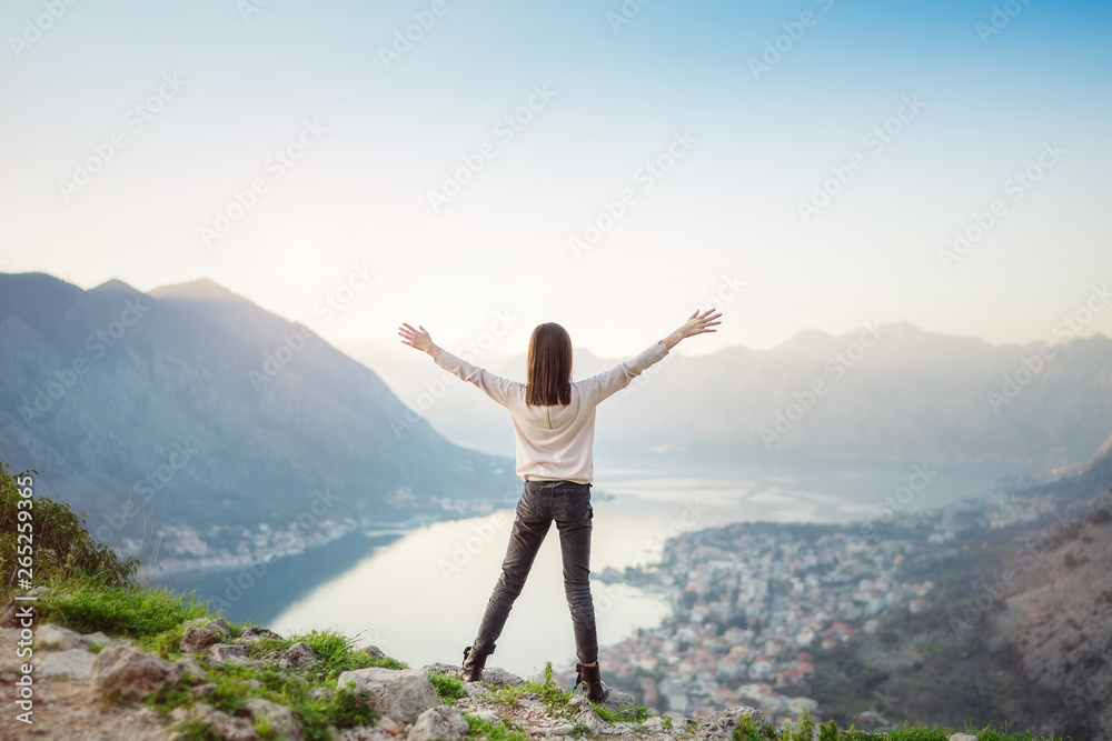 Child girl standing with raised hands above the mountain valley in a light of sunrise
