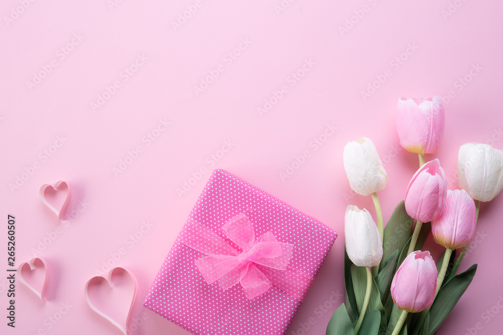 Happy mothers day concept. Top view of pink tulip flowers, gift box and paper heart on pink pastel background. Flat lay.