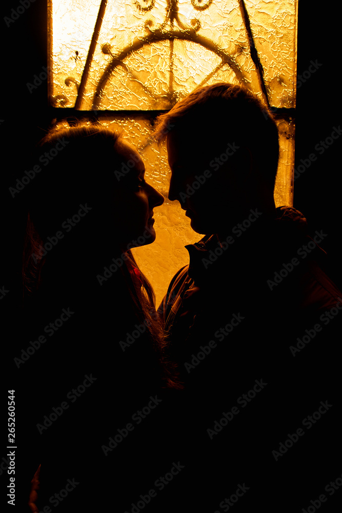 Silhouette of a loving couple. Lovers embrace in the dark. Silhouette of a guy with a girl. Photo portrait of lovers close up. Dramatic photo portrait.