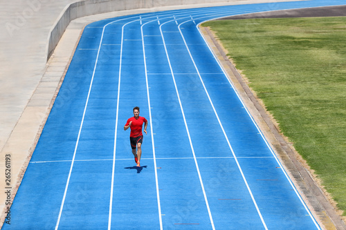 Sprinter runner athlete man sprinting on outdoor track and field running lanes at stadium. Sport and health active training on blue tracks. photo