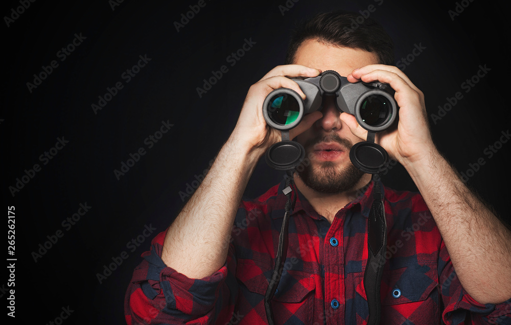 young man looking through binoculars and wondering young man looking through binoculars and wondering