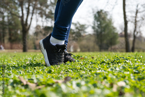 women's feet in black sneakers on the grass on the lawn on a Sunny day , sports shoes