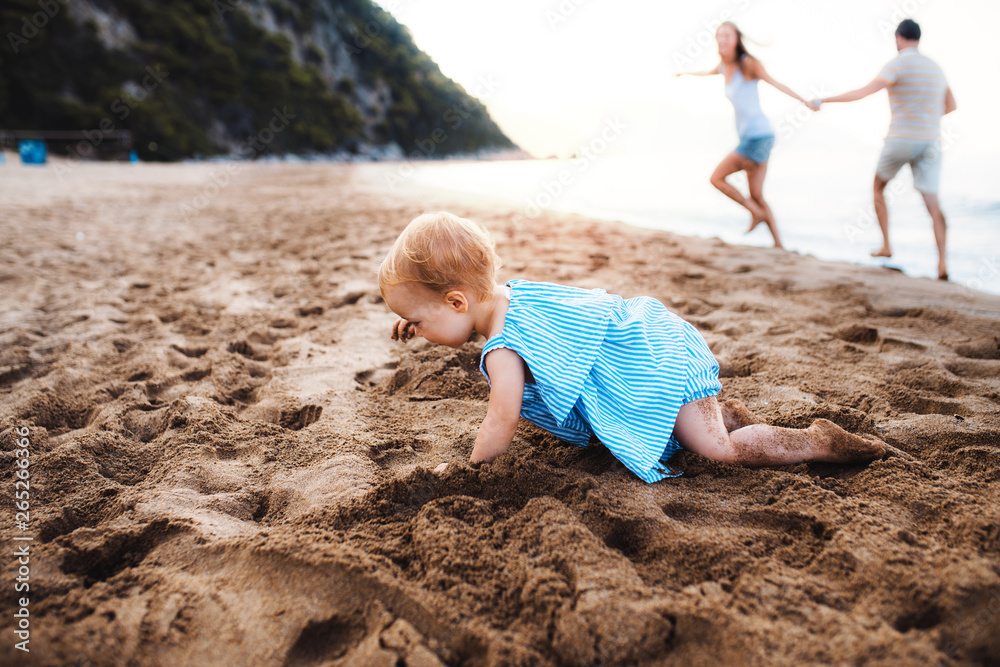 A small toddler girl playing in sand on beach on summer holiday. A small toddler girl playing in sand on beach on summer holiday.