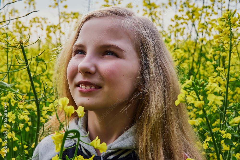 Closeup young girl happy on a sunny day in a rapeseed field, mustard with lots of yellow flowers Closeup young girl happy on a sunny day in a rapeseed field, mustard with lots of yellow flowers