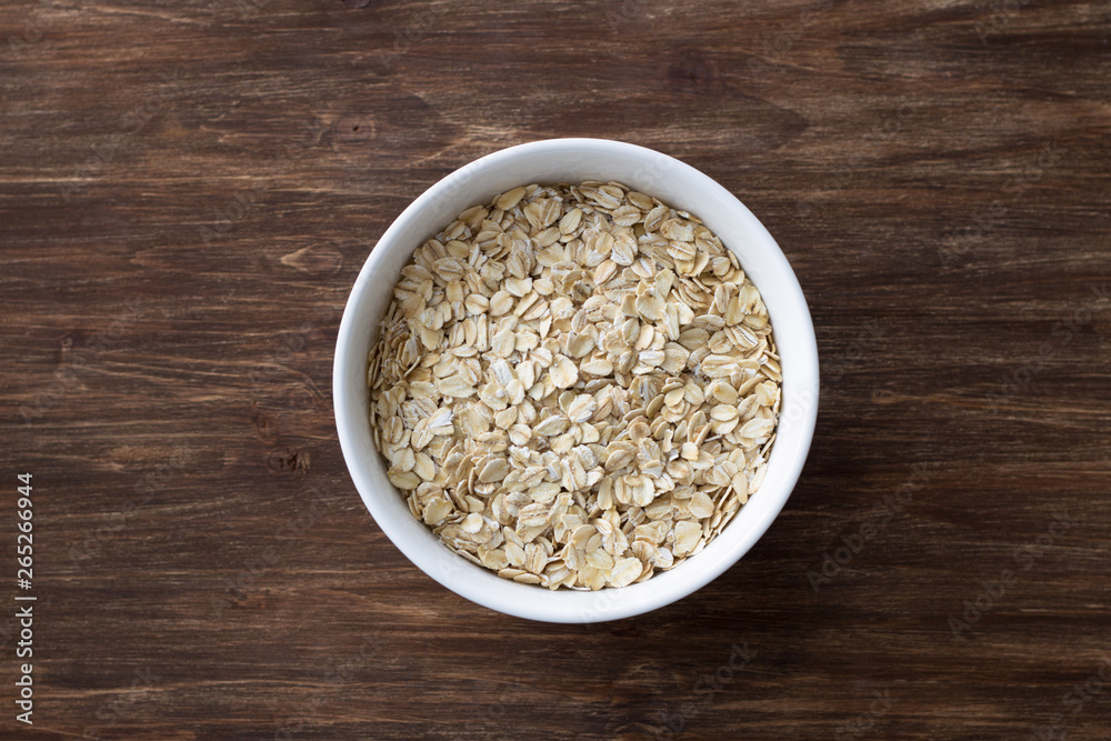 Oat flakes, rolled oatmeal in a white bowl on a wooden table Oat flakes, rolled oatmeal in a white bowl on a wooden table