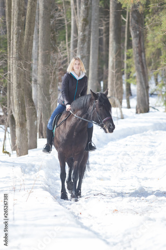 A winter forest. A young woman riding a black horse