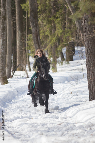 A winter forest. A woman with long hair riding a dark brown horse