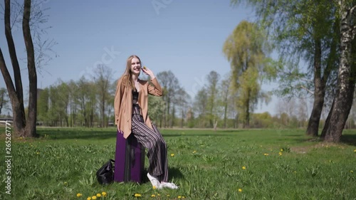 Young happy traveler arrived to new destination country - Waiting for her bus taxi - Emotions of a white caucasian female woman with light long hair wearng bra and beige jacket photo