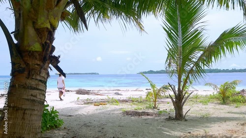 Slow motion: woman walking on sunny tropical beach caribbean sea palm trees turquoise water white sand coastline at Pulau Tailana Banyak Islands Sumatra Indonesia rear view photo