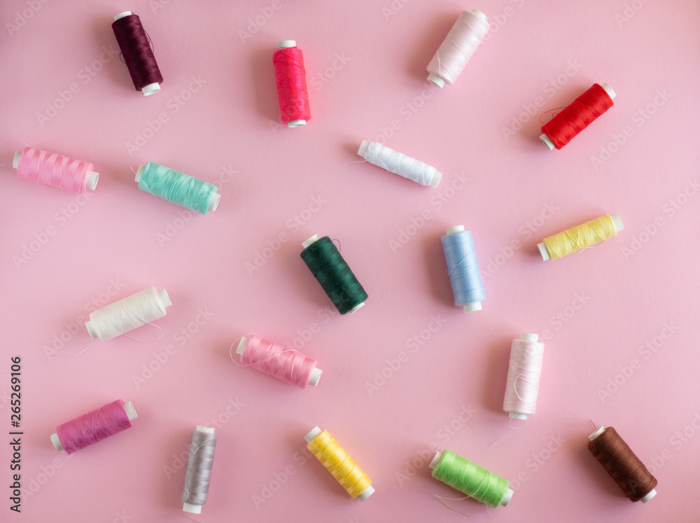 Many bobbins of bright sewing thread with a soft pink background Many bobbins of bright sewing thread with a soft pink background