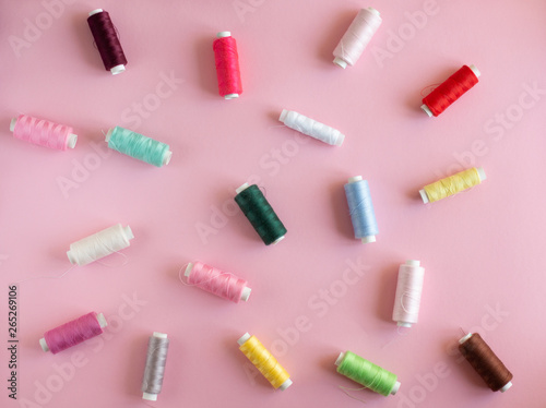 Many bobbins of bright sewing thread with a soft pink background