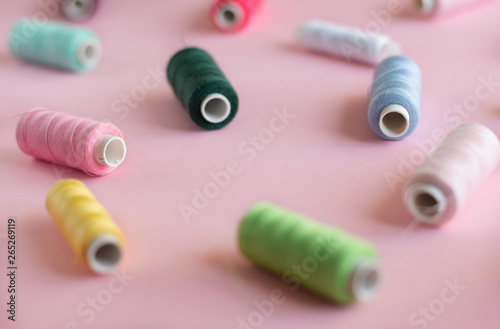 Many bobbins of bright sewing thread with a soft pink background