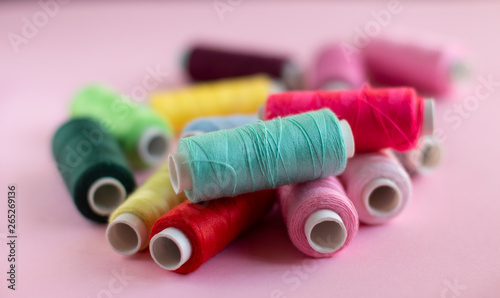 Many bobbins of bright sewing thread with a soft pink background