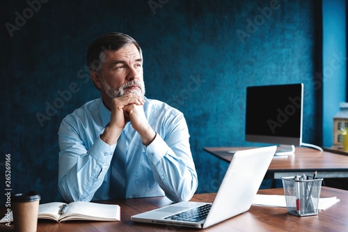 Focused mature businessman deep in thought while sitting at a table in modern office. photo
