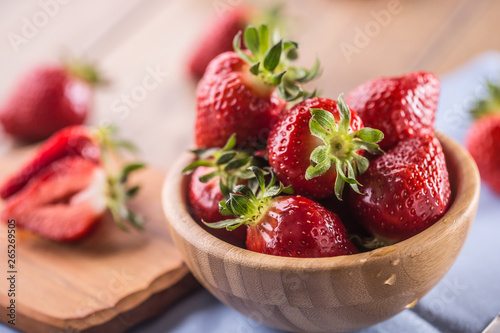 Juicy washed strawberries in wooden bowl on kitchen table