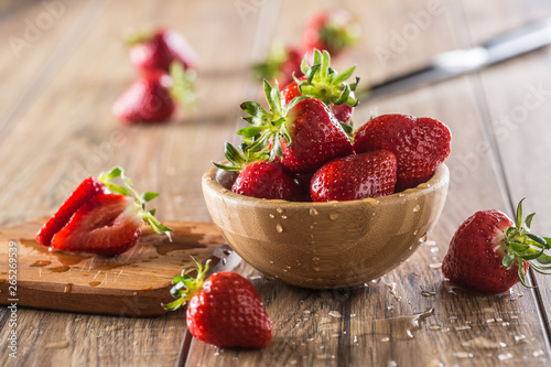 Juicy washed strawberries in wooden bowl on kitchen table