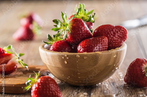 Juicy washed strawberries in wooden bowl on kitchen table