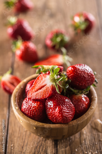 Juicy washed strawberries in wooden bowl on kitchen table