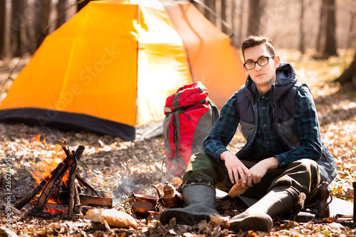 A young traveler in the forest is resting near the tent and cooked breakfast in nature