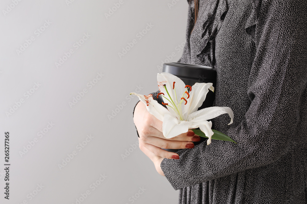 Woman with mortuary urn and lily flower on light background - obrazy, fototapety, plakaty 