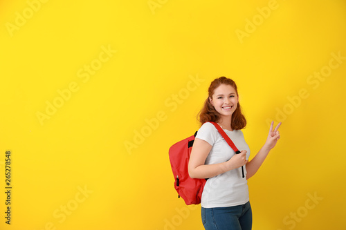 Cute teenage girl showing victory gesture on color background