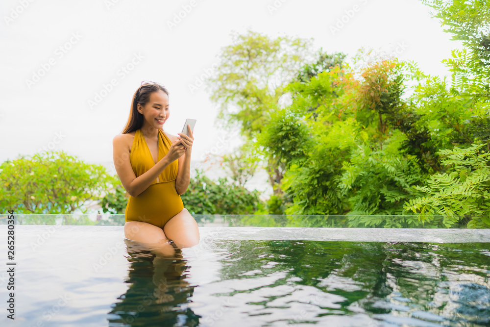 Portrait beautiful young asian woman with cell phone or mobile phone around swimming pool at hotel resort