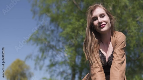 Young happy traveler arrived to new destination country - Waiting for her bus taxi and doing funny faces - Emotions of a white caucasian female woman with light long hair wearng bra and beige jacket photo