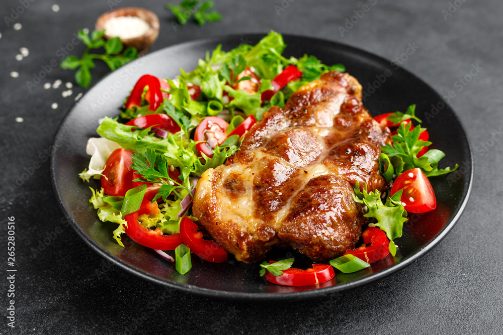 Baked pork steak with fresh vegetable salad on a plate Baked pork steak with fresh vegetable salad on a plate