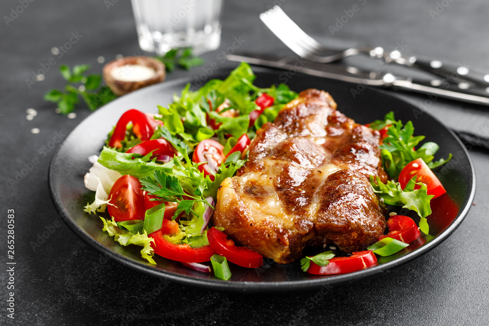 Baked pork steak with fresh vegetable salad on a plate Baked pork steak with fresh vegetable salad on a plate