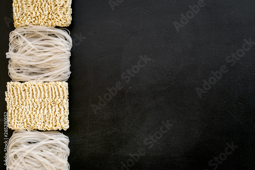 Chinese and Japanese food cooking with rice vermicelli, noodles and sticks on black background top view copyspace photo