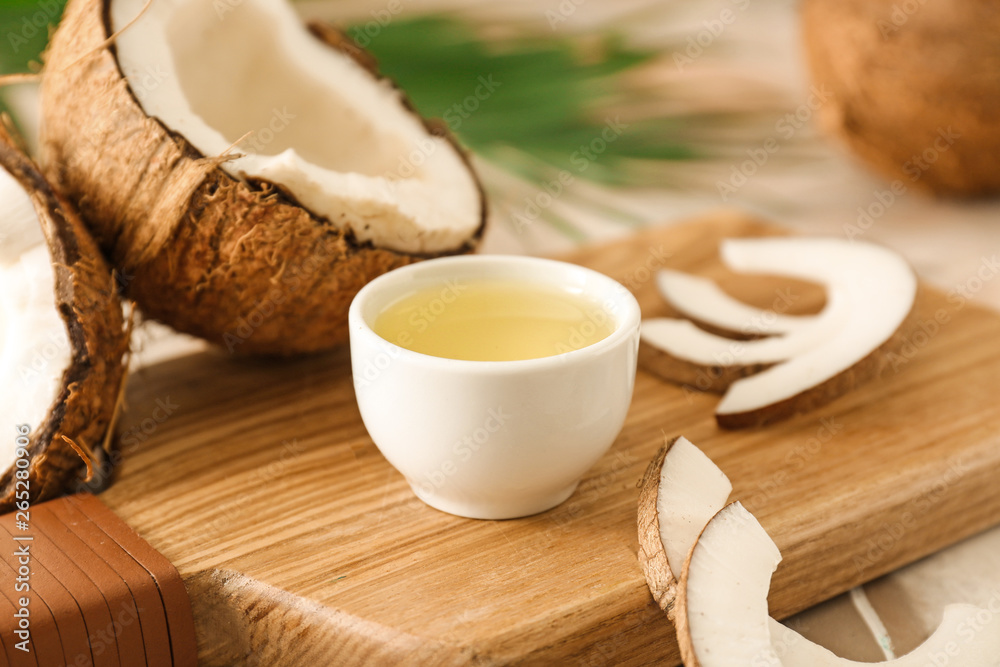 Fototapeta premium Fresh coconut oil in white bowl with cracked coconuts and flakes on wooden board, tropical ingredient for cooking and beauty
