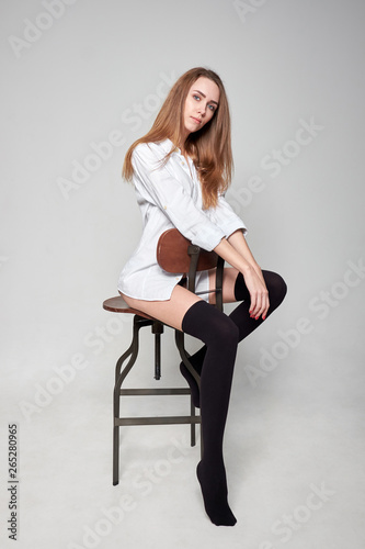 Beautiful stylish confident girl wearing a white shirt and black stockings siting on the chair.