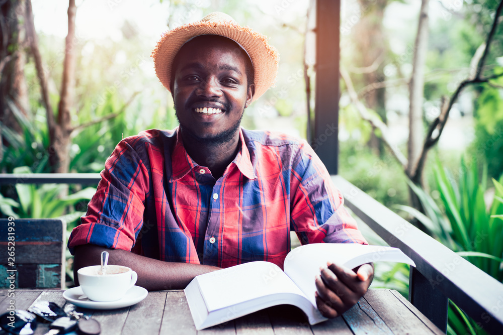 African american man reading a book with coffee , key ,smartphone and green natural background. African american man reading a book with coffee , key ,smartphone and green natural background.
