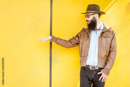 Portrait of a stylish bearded man dressed in jacket and hat on the bright yellow background outdoors photo