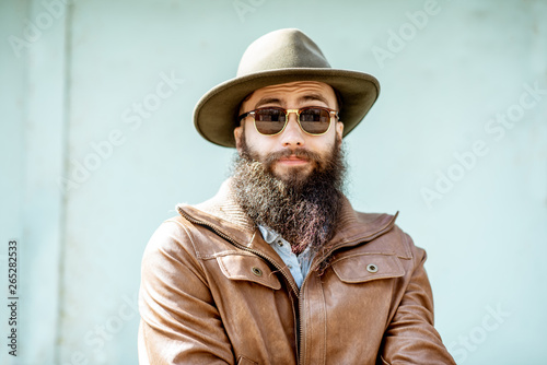 Portrait of a stylish bearded man dressed in jacket and hat on the light turquoise background outdoors photo