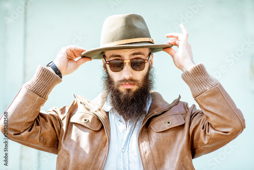 Portrait of a stylish bearded man wearing hat on the light turquoise background outdoors photo