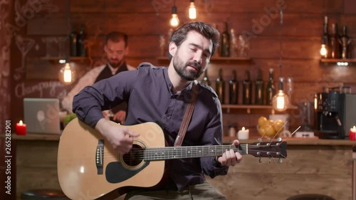 Young man performs a song on an acoustic guitar. Man plays a guitar in front of a bar counter. Singing a song in a small restaurant.
